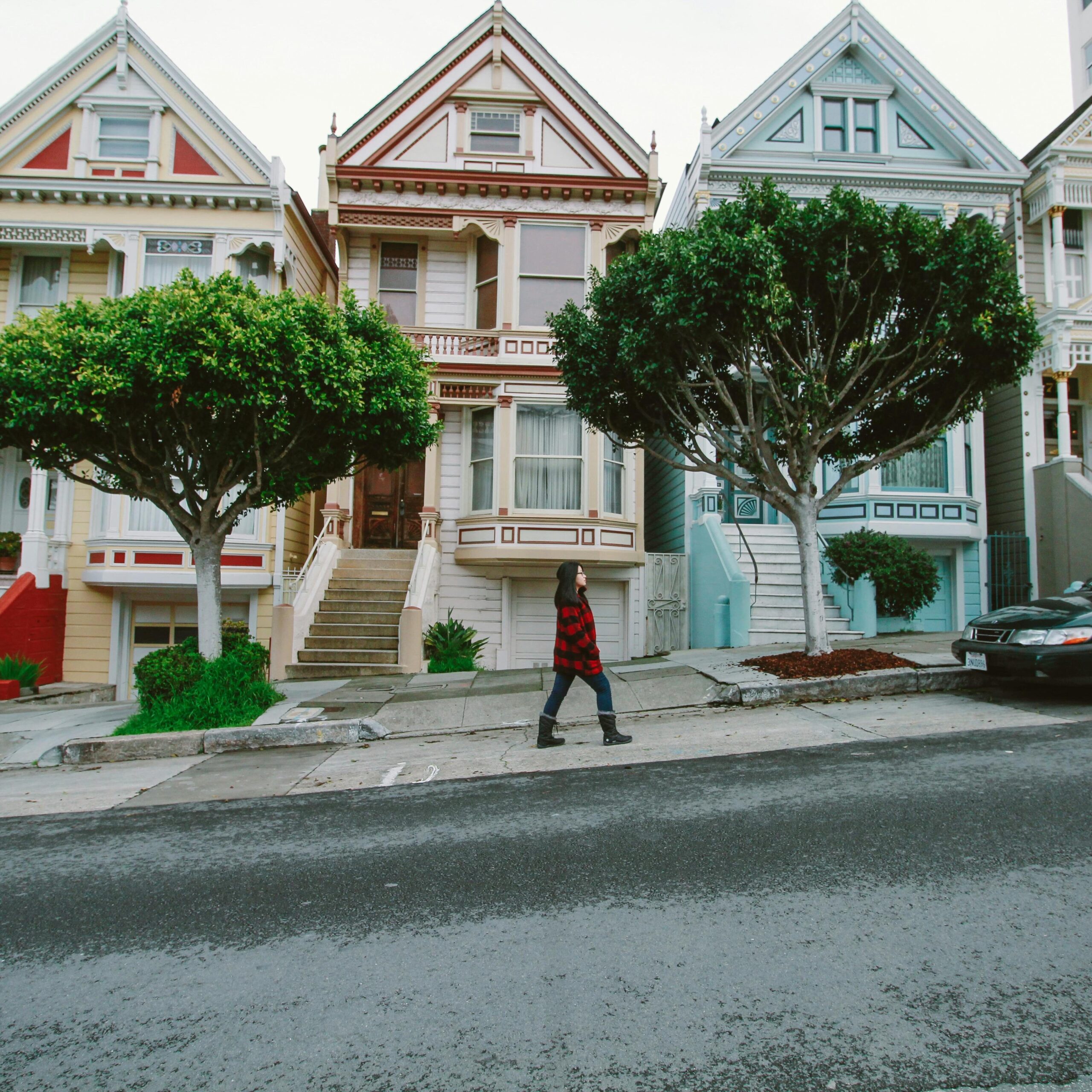 A woman walks past iconic Victorian houses in San Francisco, showcasing urban charm.